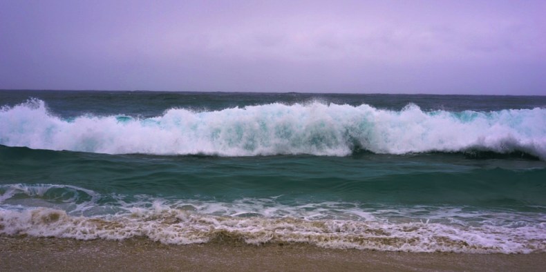 Ctrl-Break A mid-distance photograph of a powerful wave breaking on a beach, creating a line of frothy white foam. It is perfect surf weather.