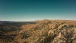 A sweeping shot of the Larapinta range in Northern Territory, Australia. The sere earth and vegetationncontrast with the sky's hint at aquamarine and beige trim.