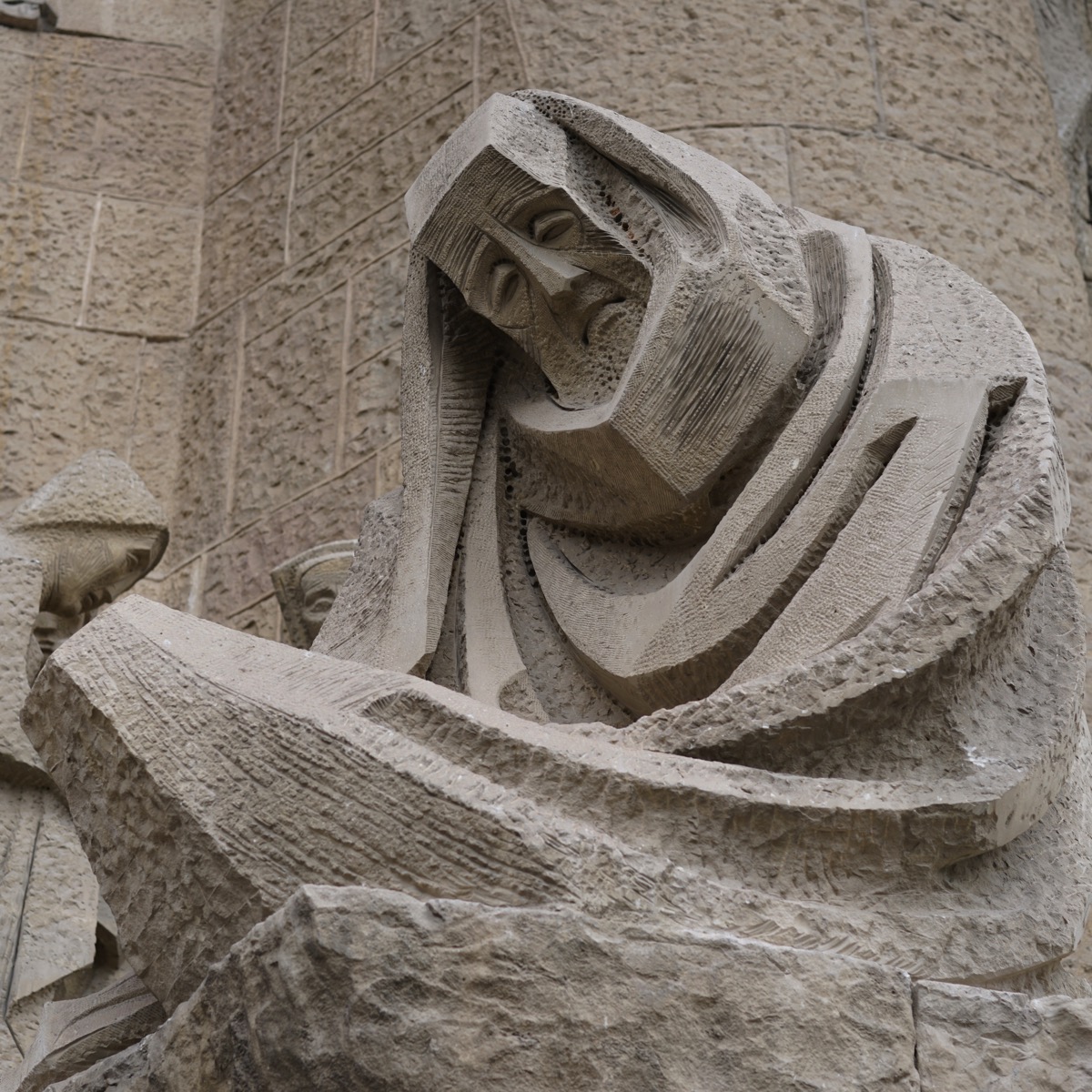 A close-up photograph of the stone sculpture 'The Weeping St. Peter' by Josep Maria Subirachs, on the Passion Façade of the Sagrada Família in Barcelona, Spain. The sculpture captures the raw emotion of a figure with his head in his hand, a posture of grief and regret that is perfectly reflected in the post's title, 'mourn'.