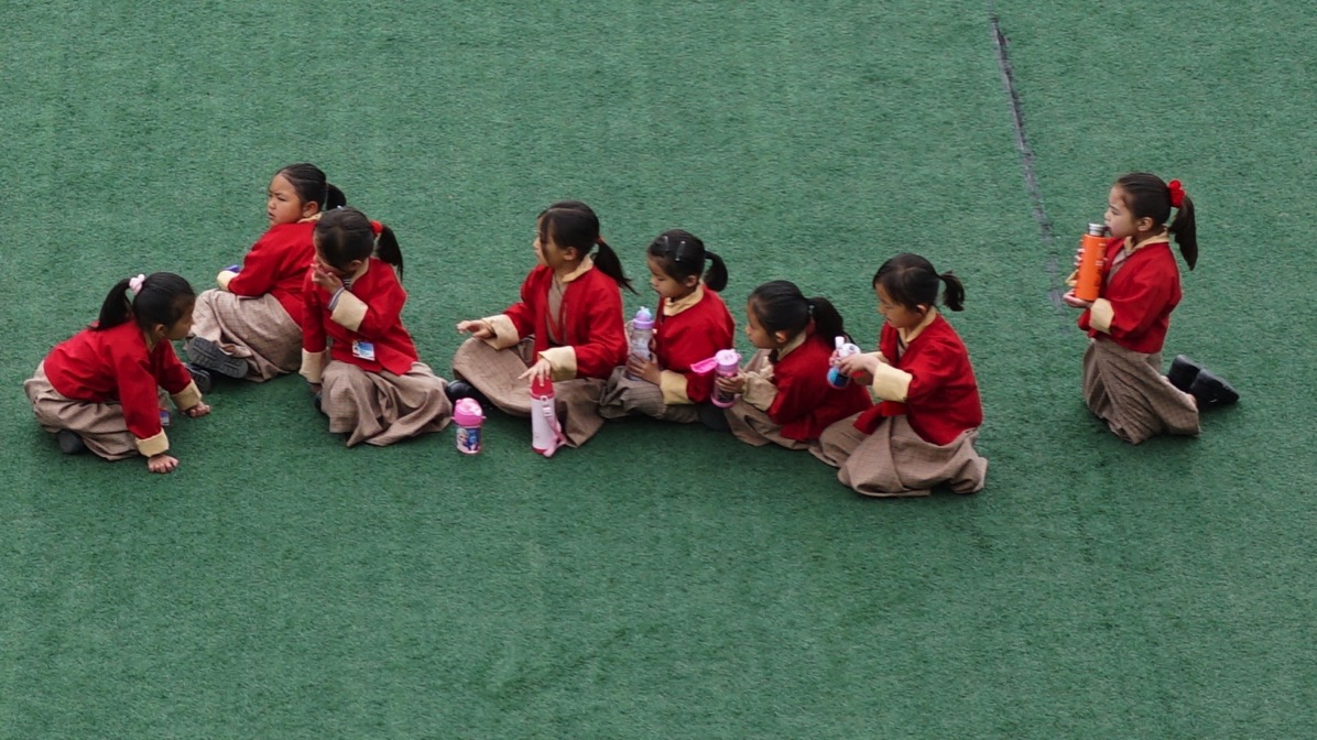 A row of Bhutanese schoolgirls clad in red uniforms on a deep green school-field.