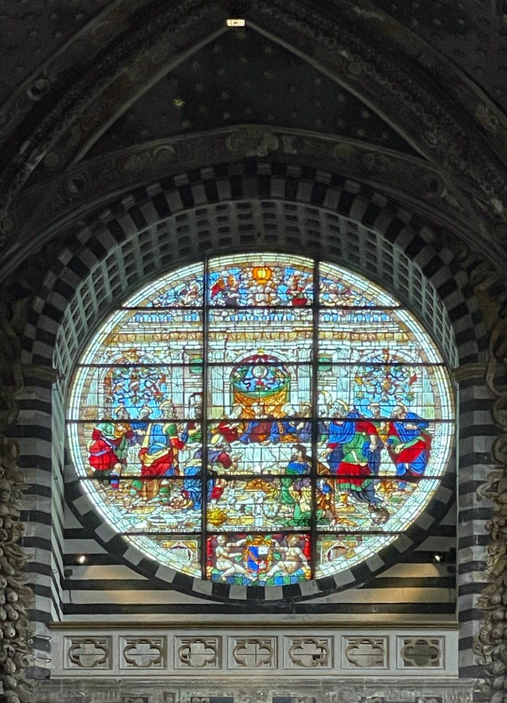 An ornate, circular stained-glass window depicting 'The Last Supper' in a beautiful mosaic of bright colors. The image's location in a cathedral or church and its unique design provide a distinct religious and artistic take on the theme of 'last suppers'.