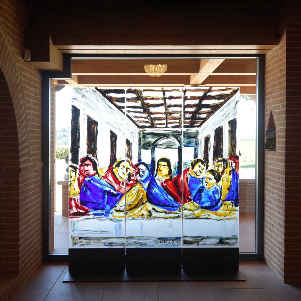 A vibrant and colorful contemporary painting of 'The Last Supper' by Christopher Lehmpfuhl, displayed in a well-lit gallery space. The artwork features abstract, expressive figures in a modern style, contrasting with the classical and traditional depictions of the same scene presented elsewhere in the post.